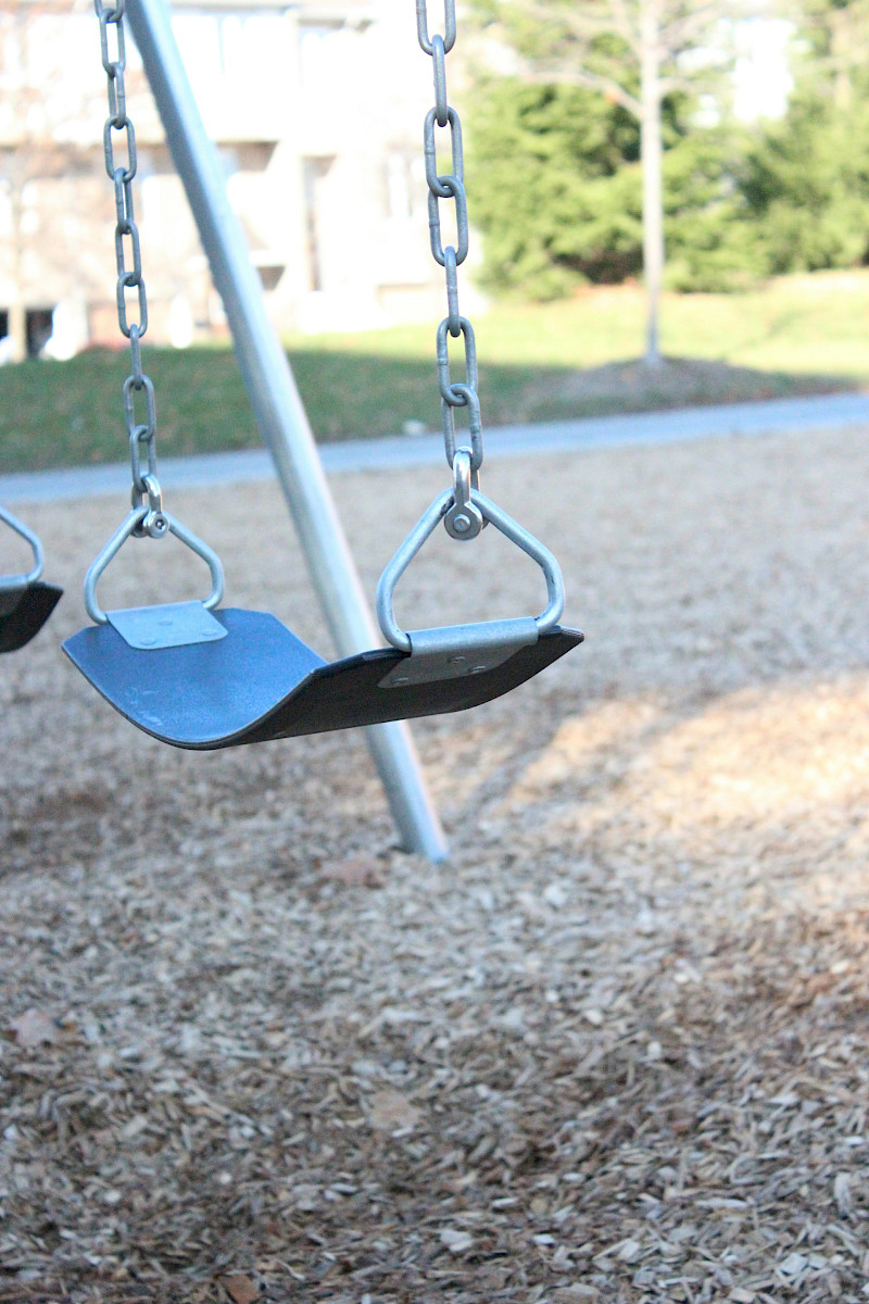 a swing set in a park with a building in the background. Photo by Ewa Anderson, Unsplash.