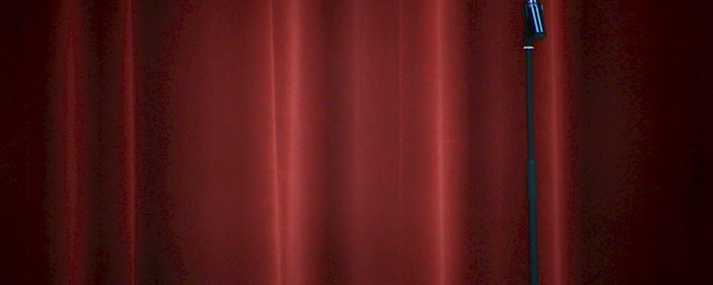 black microphone on red curtain. Photo by Joshua Hoehne, Unsplash.